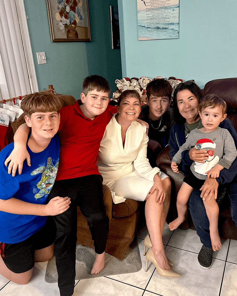 Teresa smiling and sitting on a couch with a few smiling children ranging in age